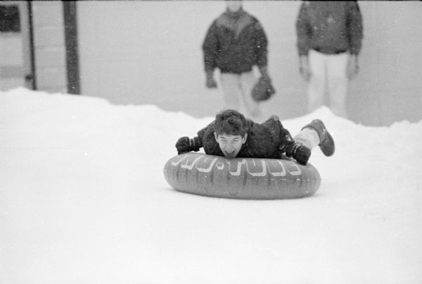 A young boy is going down a snowy hill on a Sno-Tube during the blizzard.