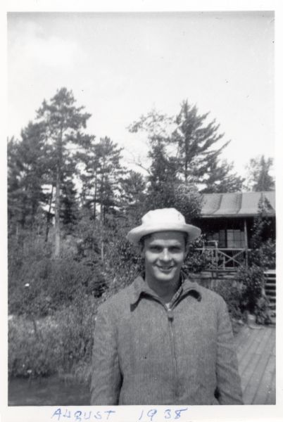 Future Wisconsin Senator, William Proxmire, wearing a coat and hat at what appears to be a rural cabin.