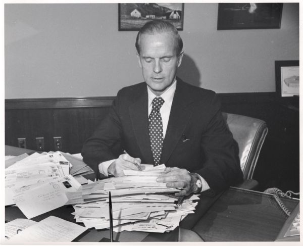 Wisconsin Senator, William Proxmire, sitting at his desk with a large stack of mail.