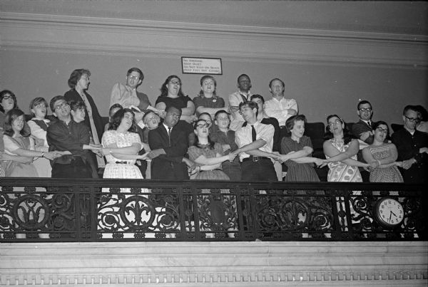 Twenty-seven members of the Congress on Racial Equality (CORE) are linking arms and singing "We Shall Overcome" in the balcony of the Wisconsin Assembly Chambers. The protest was an effort to encourage Wisconsin lawmakers to pass civil rights legislation against housing discrimination and for fair employment.