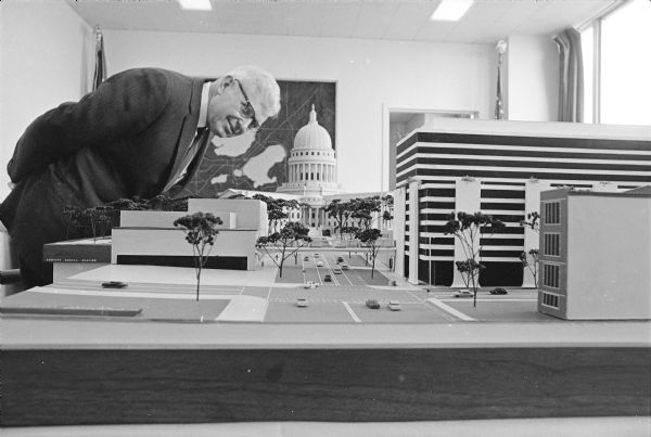Madison Mayor Henry Reynold examines a model of the Capitol Square area showing a proposed skywalk from Manchester's Department Store over Wisconsin Avenue to a proposed parking facility with office space and a motel.