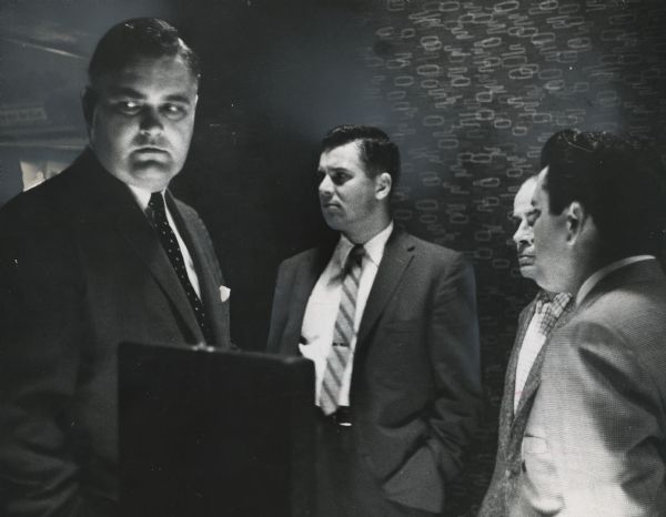 Four men are standing in a room with dim lighting. Caption reads: "<b> Checking on charges</b> of inadequate lighting, a group of city officials Thursday visited the Holiday House, 620 E. Clybourn st. They were (from left) Civil Judge Robert M. Curley, Police Sgt. Jerome Jagmin and Erwin Rathenmaier of the building inspector's office. At far right was John Volpe, licensee of the Holiday House. Judge Curley dismissed the charges Friday. A city ordinance requires adequate lighting in taverns."