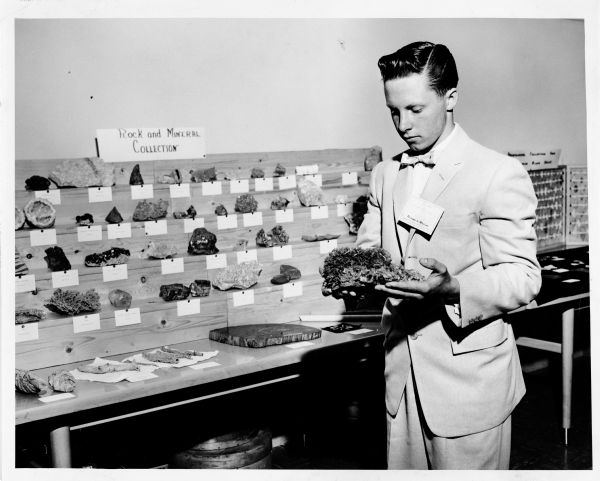 A young man is standing at a rock and mineral collection display, holding a mineral.