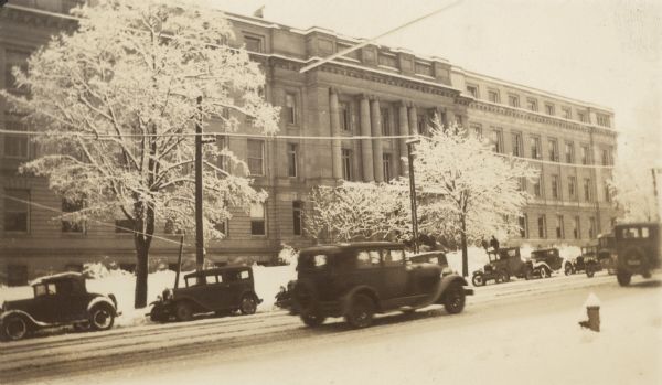 View across street towards the U.W. Chemistry Building. Automobiles are parked on the other side of the street, and snow is on the ground.