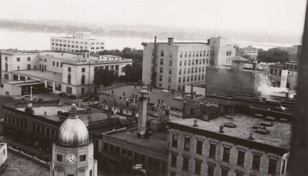 Handwritten on back: "From 10th floor of Tenney Building." There is a clock tower and dome on the building in the foreground along Pinckney Street and King Street on the left. There are other commercial buildings along Pinckney Street, and the Madison Municipal Building along East Wilson Street. Lake Mendota and the far shoreline are in the distance.