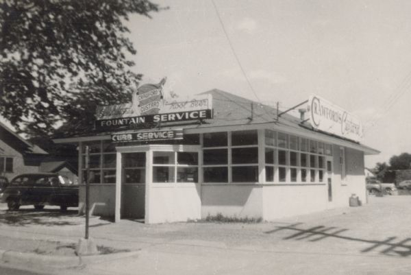 View from street towards the front of Crawford's Custard. The sign in front reads "Fountain Service" and "Curb Service." A car is parked on the left side of the building.