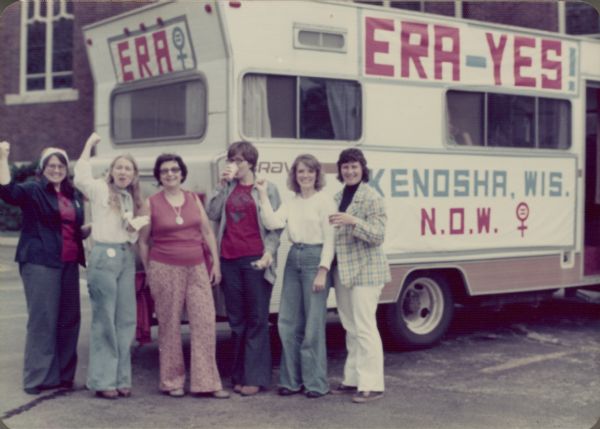 A group of women are standing together in front of a camper-van? Signs on the side and back of the vehicle read: "ERA," "ERA-YES!" and "Kenosha, Wis. N.O.W."