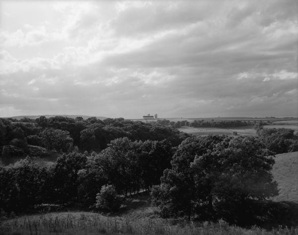 Slightly elevated view across fields and small patches of woodlands. A barn is on a hill in the distance, and there are cows in a field below on the right. Caption reads: "Mt. Horeb (vicinity), Wis. Sept. 11, 1960. View over scattered woodlands and distant fields at sundown."