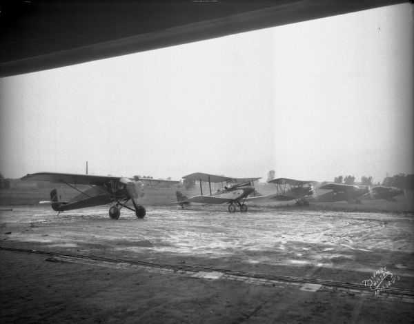 View from building towards five airplanes, parked in a line outdoors, at Madison Airport, Coolidge Avenue between North Street and Kedzie Street.