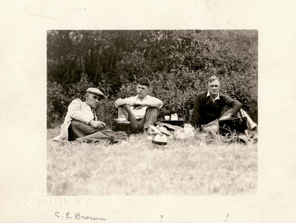 Charles Brown and two other men are sitting on the grass at the Shermer Indian Village site.