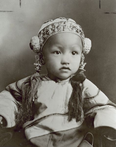 Photograph of Anna May Wong as a small child of eighteen months. She is wearing a traditional Chinese robe and headpiece.