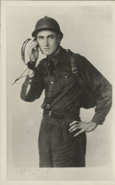 Posed portrait of Wisconsin man John Cookson wearing a helmet and holding a radio headset to his ear. This was during the Spanish Civil War.