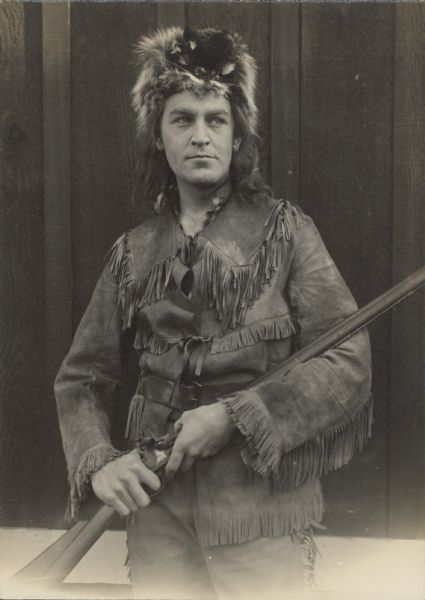 Allan "A.D." Sears portrays David Crockett in the 1915 film "Martyrs of the Alamo". He wears fringed buckskin jacket and pants as well as a fur hat while holding a rifle.