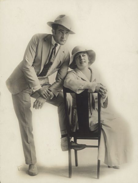 Francis Ford stands next to and leans towards Grace Cunard who sits in a chair. Cunard and Ford co-wrote, co-directed and co-starred in the Universal serial "The Purple Mask".