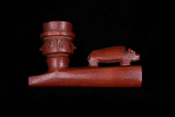 Tay-che-gwi-au-nee, a member of an Ojibwe band from the south shore of Lake Superior, presented this pipe to Wisconsin's territorial governor James Duane Doty on behalf of his father, Chief Buffalo. Doty received the gift on February 12, 1844 at a council held at Fort Winnebago, Wisconsin, near present day Portage. Half of the pipe stem is carved with round and rectangular shapes, their inner surfaces painted red. The coloring of the pipe today appears muted due to fading over time. The heavy pipe bowl is carved from the stone catlinite, quarried near the town of Pipestone in southwestern Minnesota. The relatively soft siltstone can be hand carved and drilled with stone or metal tools. One end of the pipe bowl has a carved figure commonly known as a Janus head, which represents two human faces pointing in opposite directions. On the bowl’s anterior ridge is carved a representation of a bison, which is a common symbol carved on pipes. 