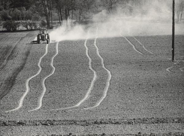 Slightly elevated view of a man driving a tractor across a field, sending dust clouds into the air. Caption reads: "Dry fields were evident as a farmer prepared a field for planting west of West Bend on Highway 33".