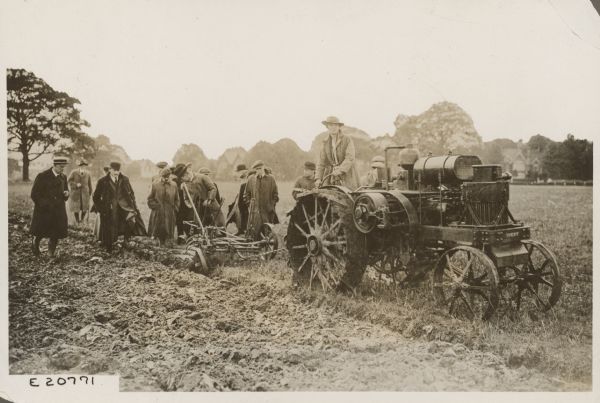 A woman is driving a tractor, which is pulling an implement. Several people are looking on. Caption reads: "Test of 8-16 H.P. [horsepower] Avery Tractor in progress at Birmingham, England. A test meeting for women war workers of the Midland Counties took place at Birmingham, England. Certificates were granted to proficient entrants in the various classes. WOMEN ARE LEARNING TO OPERATE TRACTORS IN THIS COUNTRY WITH A GREAT DEAL OF PROFICIENCY."
