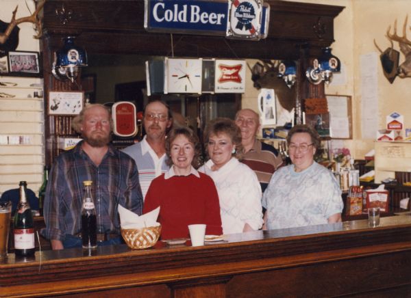 Group portrait of people standing behind the bar. Left to right are: Tom Wittnebel, James Wittnebel, Barb Lund (Wittnebel), Joyce Like St (Wittnebel), Roy Wittnebel and Lorraine Wittnebel.