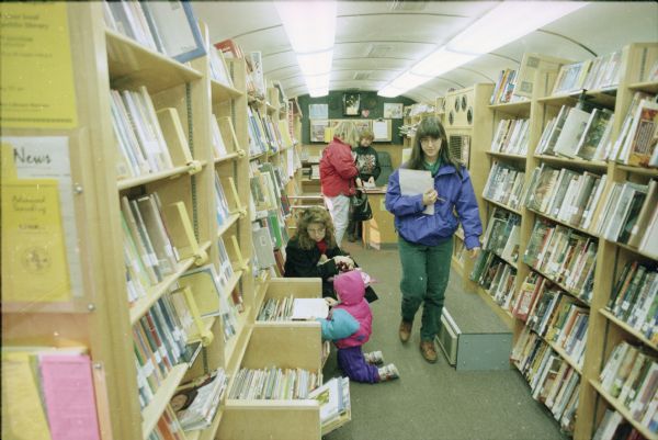 Patrons inside the Dane County Library Service Bookmobile. Cathy Bloom (in black sweater) assists a patron at the back desk.