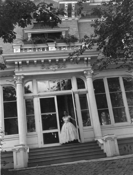 Young woman in a period dress standing at the front entrance of Villa Louis.
