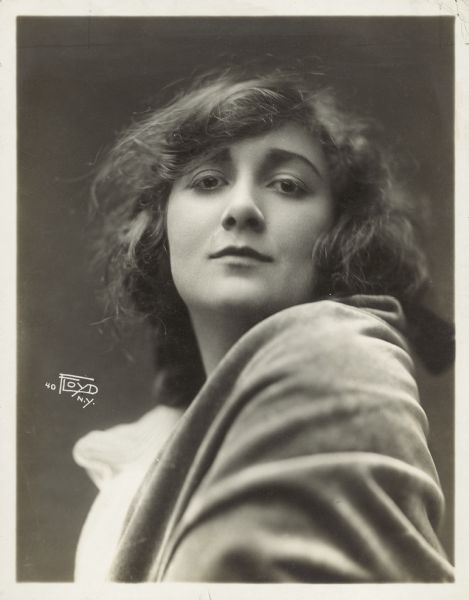 Portrait of actress Mary Fuller. Fuller sits with her shoulder towards the camera and looks down towards the camera. The handwritten caption on the back reads: "Miss Fuller possesses a natural hauteur which does not at all detract from her charm". 