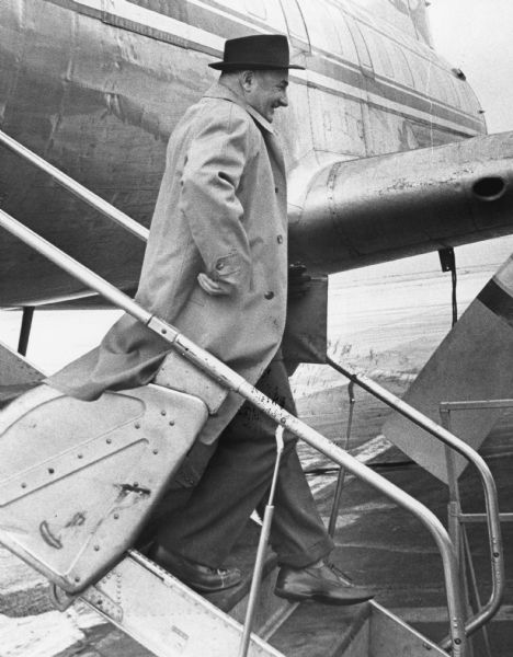 A man in a coat and hat is walking down the airstairs of a plane. Caption reads: "Andrew Depta, of Cable (Bayfield county), set a Gen. Mitchell field record Thursday when he stepped off a North Central Airlines plane and became the one millionth passenger in a year, the first time in the airport's history that figure had been reached."
