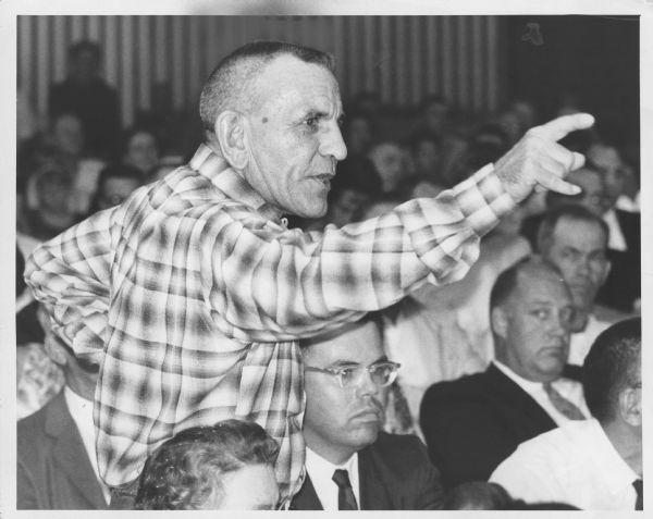 A man is standing among several seated men with his arm raised and pointing a finger. Caption reads: "<b>Royal Trabbold,</b> 4016 W. Calumet rd., pointed a finger in protest against a political speech at the Granville "freedom rally" Wednesday night in Granville high school. Trabbold insisted that the discussion should be limited to the annexation of Granville by Milwaukee. Story on page 1."