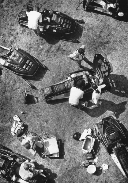 Overhead view of people with six snowmobiles in a grassy field. Caption reads: "Drivers and crew members prepared their machines for the races.
It's a little early for snow, even in Wisconsin. But that didn't stop the snowmobile racers who put their machines to the test at the Reichard Cup Snowmobile Grass Drag Championships recently at Reichert Sports, W188-N10707 Maple Rd., Germantown. The races featured fast machines racing on a grass track, as well as refreshments for the crowd who packed the areas along the fences to watch."