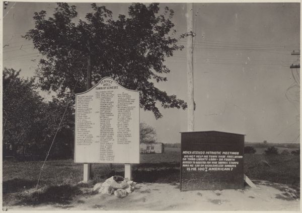 View of the service roll for the Town of Genesee. Local service members' names are listed, and a small cannon is set up below. Next to it is a sign that reads: "Never attends patriotic meetings Did not help his town raise First, Second, or Third Liberty Loans — or Fourth Refused to register for war savings stamps Runs his car on Gasoleneless Sundays. IS HE 100% AMERICAN?"
