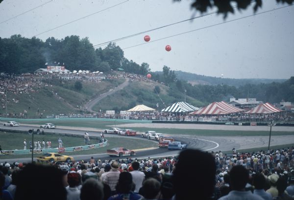 View from the stands of an automobile race at Road America near Elkhart Lake. Large striped tents are in the background on the right.
