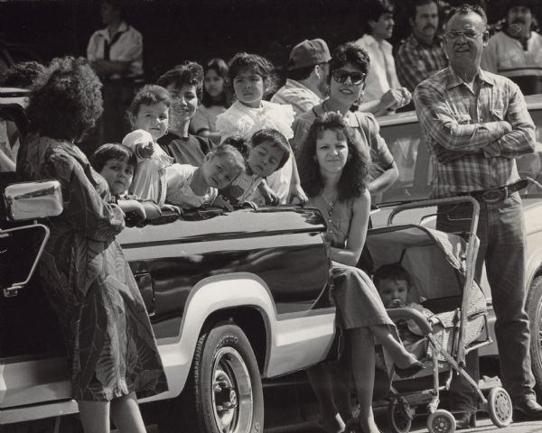 A group of people are standing and sitting, including several children in the back of a truck. Caption reads: "Spectators lined the Mexican Independence Day parade route Sunday to watch a multitude of marching bands and floats. The parade and festival that followed celebrated Father Miguel Hidalgo's call to arms on Sept. 16, 1810, which eventually resulted in Mexico's freedom from Spanish rule in 1921."