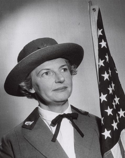 A woman is posing in a hat and costume next to an American flag. Caption reads: "<b>Mrs. Charles Harrison,</b> N. Harcourt pl., portrayed a member of the 1917 League of Patriotic Women for the Thursday program at the Woman's Club of Wisconsin. Members of the welfare committee gave a skit depicting charity work initiated by the club through the years. Thursday's meeting was the 80th birthday party for the club."