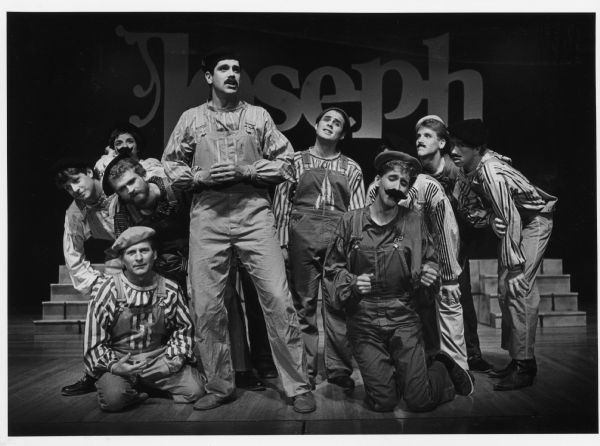 Ten people posing on stage, in costume. On the curtain behind them is the word Joseph. Caption reads: "TECHNICOLOR DREAMCOAT — The Village Players of Mukwonago are presenting 'Joseph and the Amazing Technicolor Dreamcoat' at Mukwonago High School tonight, tomorrow and next Thursday, Friday and Saturday. In this scene, Reuben (standing in the foreground and played by Pat Berigan of Wauwatosa) is signing [sic] to his brothers. Reservations can be made by calling 363-5804. Curtain time is 8 p.m."