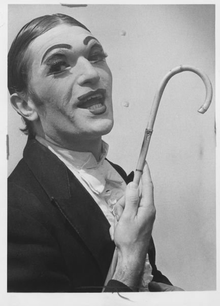 A man in costume — including greasepaint and exaggerated eyebrows and lips — posing holding a cane. Caption reads: "Charles Abbott, dressed for his role as the master of ceremonies in the musical 'Cabaret,' prepared to go on stage on opening night Monday at the Palace theater. The play is running in Milwaukee through Saturday."