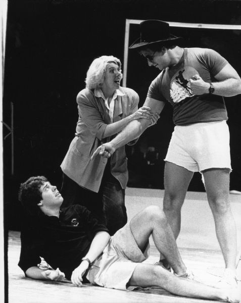 View of a stage rehearsal. A man is standing and pointing at a man who is lying on the stage. A woman is grabbing the standing man's arm. Caption reads: "SUMMMER SHOW — Andy Jesse, A. Beth Frost and Gilbert Salm rehearsed a scene from 'The Best Little Whorehouse in Texas' for Port Summer Theatre's 20th season of plays. The performances will be [sic] the Port Washington High School auditorium, 427 W. Jackson St. The play will be presented at 8 p.m. July 21-22 and July 27, 28 and 29. Tickets are $5 at the door, $4 in advance from cast members or at Port Apothecary."