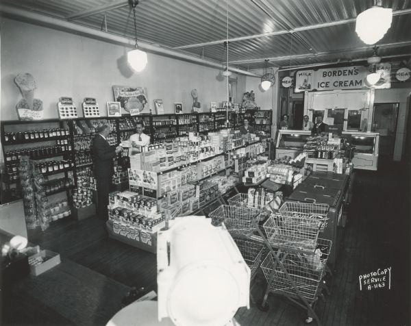 McConley's Food Market, interior, 1254 East Washington Avenue, showing counter with scale, shopper carts, shelves of canned goods, refrigerator in rear, Borden's Ice Cream sign, milk and meat signs, four men and two women. Taken for Kennedy-Mansfield Dairy Company.