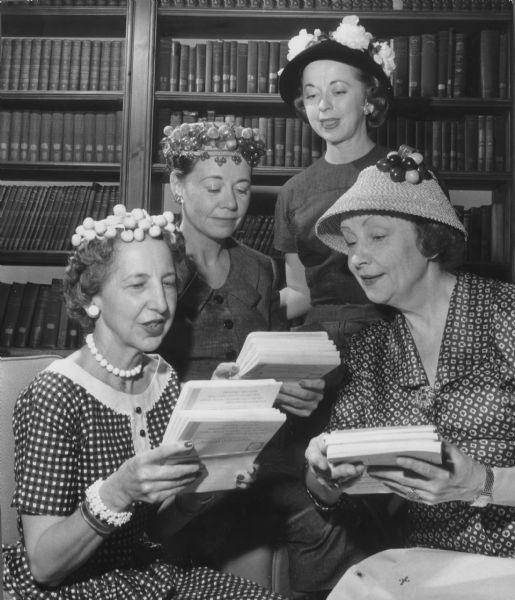 Four women posing in front of bookshelves, looking at stacks of publications. Caption reads: "<b>The Theater Guild committee</b> met Wednesday at the University club to plan its fall campaign. A permanent committee of 200 will work for the guild's subscription series. The guild plans to present five plays during the winter season. From left are Mrs. Herbert [Grace Rubena Newby] Dallwig, 2209 E. Kenilworth pl.; Mrs. Richard M. Davis, 7100 N. Lake dr., Fox point, chairman of the group; Mrs. Edward J. Rogers, 10108 W. Meinecke av., Wauwatosa, and Myrna Peache, 1007 N. Van Buren st., manager of Pabst theater."