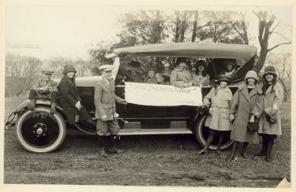 Eleven children posing around an automobile. A banner on the car reads: "'The Butterfly Kiddies' Welton Co. 245 Ac."