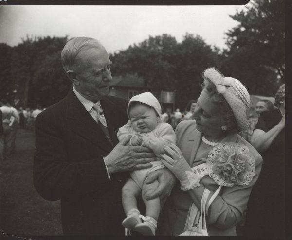 A man is holding an infant in his arms. A woman standing next to him also has her hand on the infant. Caption reads: "Celebration for Dr. [Arthur W.] Jones' 50th year of practice at Randolph Wis 1951".