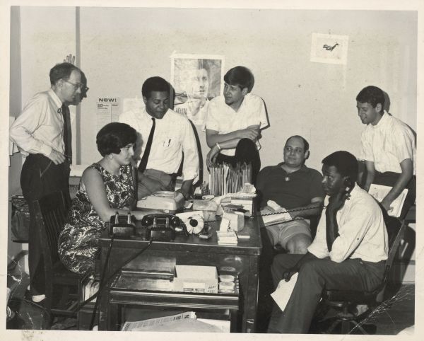 George Wiley is sitting around a desk with other members of the National Welfare Rights Organization (NWRO). The man who is sitting on the right is talking on the telephone.