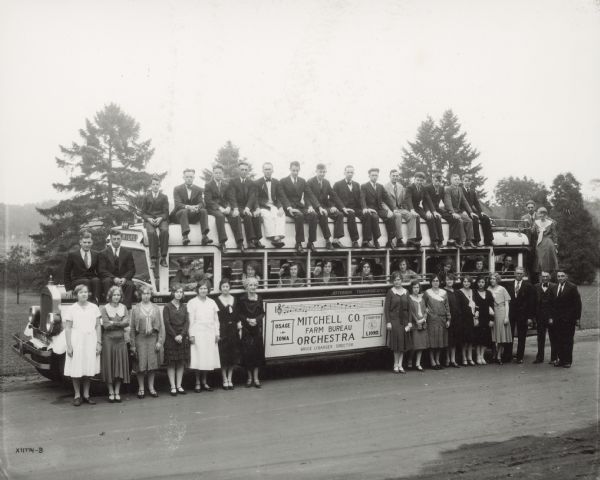 22 men and 22 women posing in and around a bus, which has a sign on the side that reads: "Mitchell Co. Farm Bureau Orchestra, Bruce Lybarger, Director. Osage, Iowa. Courtesy, Lions." It includes musical notation for part of the George E. Hamilton's "Iowa Corn Song." 