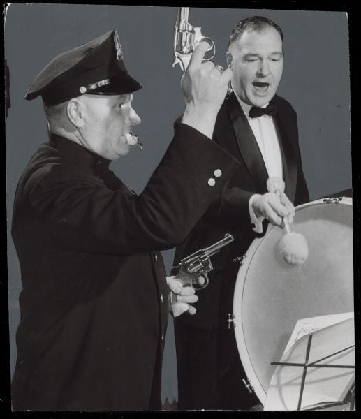 A uniformed policeman is blowing a whistle and holding two revolvers, next to a man playing a bass drum. Caption reads: "<b>Some of the sound effects</b> for one composition at the Milwaukee Pops teen age concert Friday night at the vocational school will be supplied by Patrolman Raymond Morawetz, who will fire shots and blow a police whistle. A siren has been borrowed from the Glendale fire department for the concert. Morawetz was coached at rehearsal by his brother, Edward Morawetz, 4321 N. 19th st., Pops' bass drummer."
