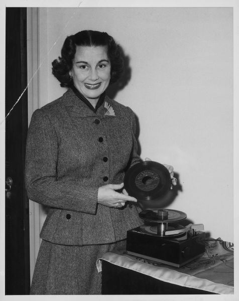 A woman is holding a record next to a record player. Caption reads: "RCA Victor's new 7-inch, non-breakable vinylite 45 RPM record and its component record playing attachment is demonstrated by opera and concert star Gladys Swarthout, who declared that 'the new RCA Victor record and record player produce a beauty and fidelity of tone which I never believed could be achieved by recorded music.'"