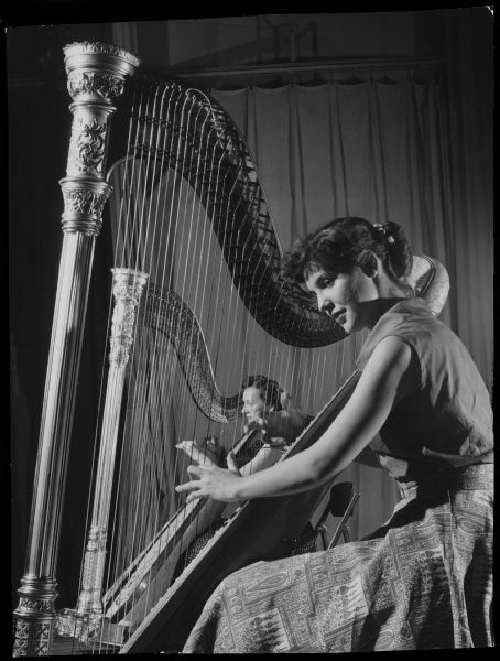 Two women playing harps. Caption reads: "<b>Auditions for the new Milwaukee Pops orchestra</b> were held Saturday at Radio City. Miss Carol Dahm (front), 2956 N. Hackett av., and Mrs. Kitty Westerlund, 2642 N. Farwell av., played harps. Altogether, 35 musicians tried out. The three judges announced no winners. Of 66 positions in the orchestra, 30 already have been filled."