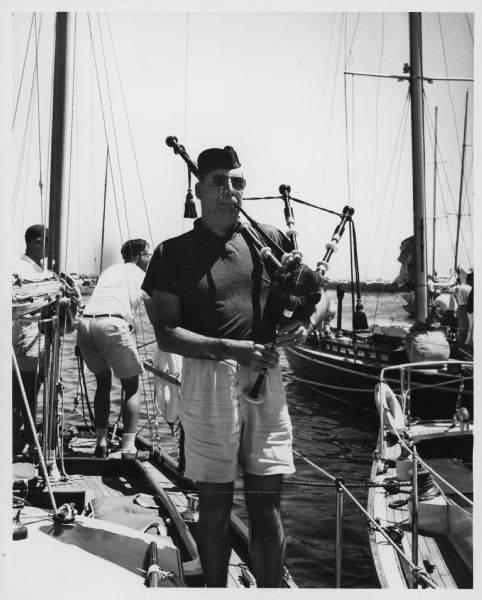 A man playing bagpipes on the deck of a boat. Caption reads: "<b>When the big sailboat fleet</b> docks at a Lake Michigan port after a race, startled salts are likely to hear sounds which might have been emitted by a pinched pig. Here is the cause, bagpiper Fred Lewis of St. Johns, Mich. The attorney is a regular crew member aboard the yacht Rarotonga of Macatawa, Mich., and he has been tootling on the pipes for six years. The racing fleet was docked at Milwaukee's South Shore Yacht club when Lewis squealed out this number, a reel entitled 'The High Road to Linton.'" 