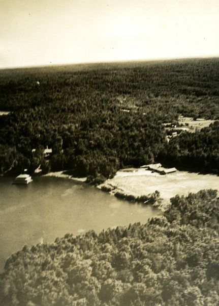 Aerial view of the cow palace and pasture, the boathouse, and the Lake Namakagon shoreline. The main lodge is barely visible among trees. Old highway county D (now Garmisch Road) is in the distance, as well as the additional property on the other side of county D.