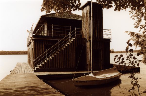 Large two-story vertical log boathouse with an elevator shaft, located on Lake Namakagon. A small sailboat is tied to the boathouse dock.