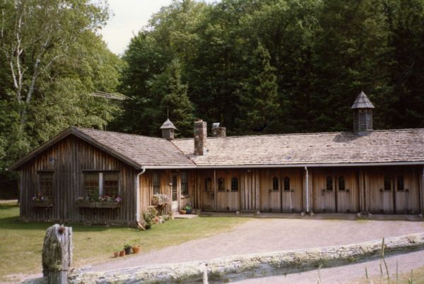 The Cow Palace, a wooden cow barn and apartment at Forest Lodge on Lake Namakagon. Flower boxes are situated on the apartment portion of the cow palace. The cow palace is roofed with cedar shingles and has three cupolas and two chimneys.