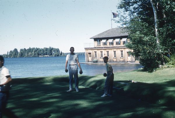 Three boys lawn bowling on the bowling green next to Lake Namakagon; the Forest Lodge Boathouse and Champagne Island are in the background.