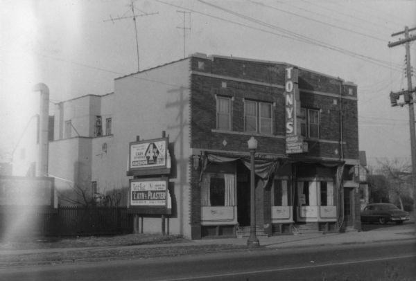 Exterior front view from left of Tony Urso's Westside Palm Tavern located at 730-736 West Washington Avenue in the Greenbush neighborhood. There are two billboards on the left side wall of the building. Typewritten sheet with photograph reads: "This is a very well built building with a large dining room and bar on first floor with a restaurant kitchen in the same building since 1912. Building has been remodeled several times and is in good condition, has recently been equipped with new aluminum combination screens and storms."